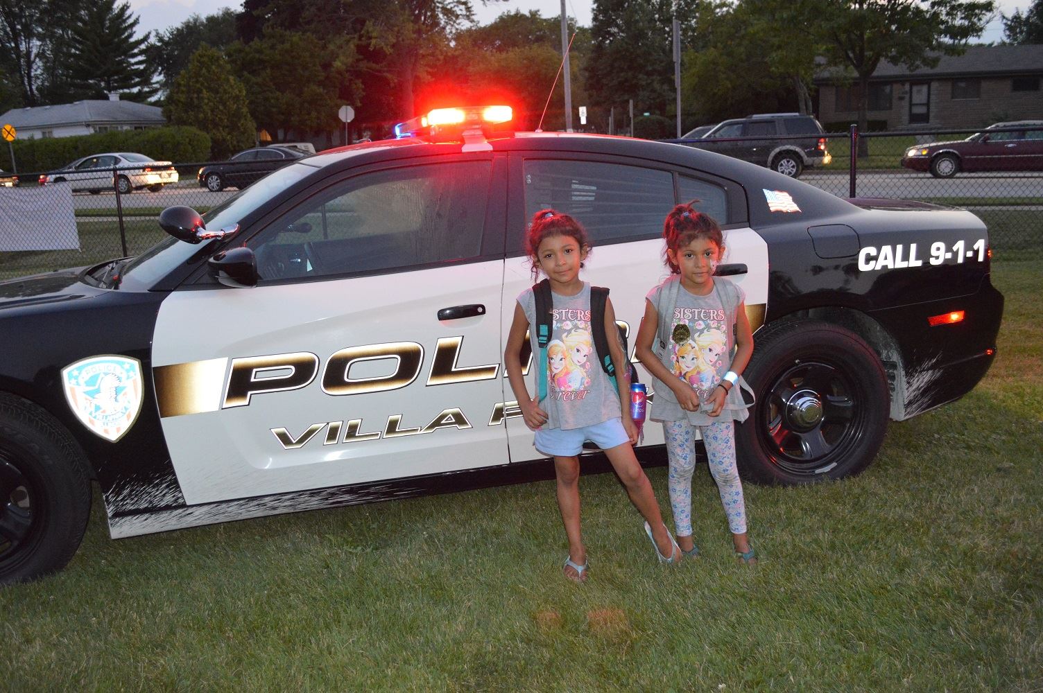 Two young girls pose for a photo in front of Villa Park Police car at a National Night Out event at the Iowa Community Center, Aug. 2.